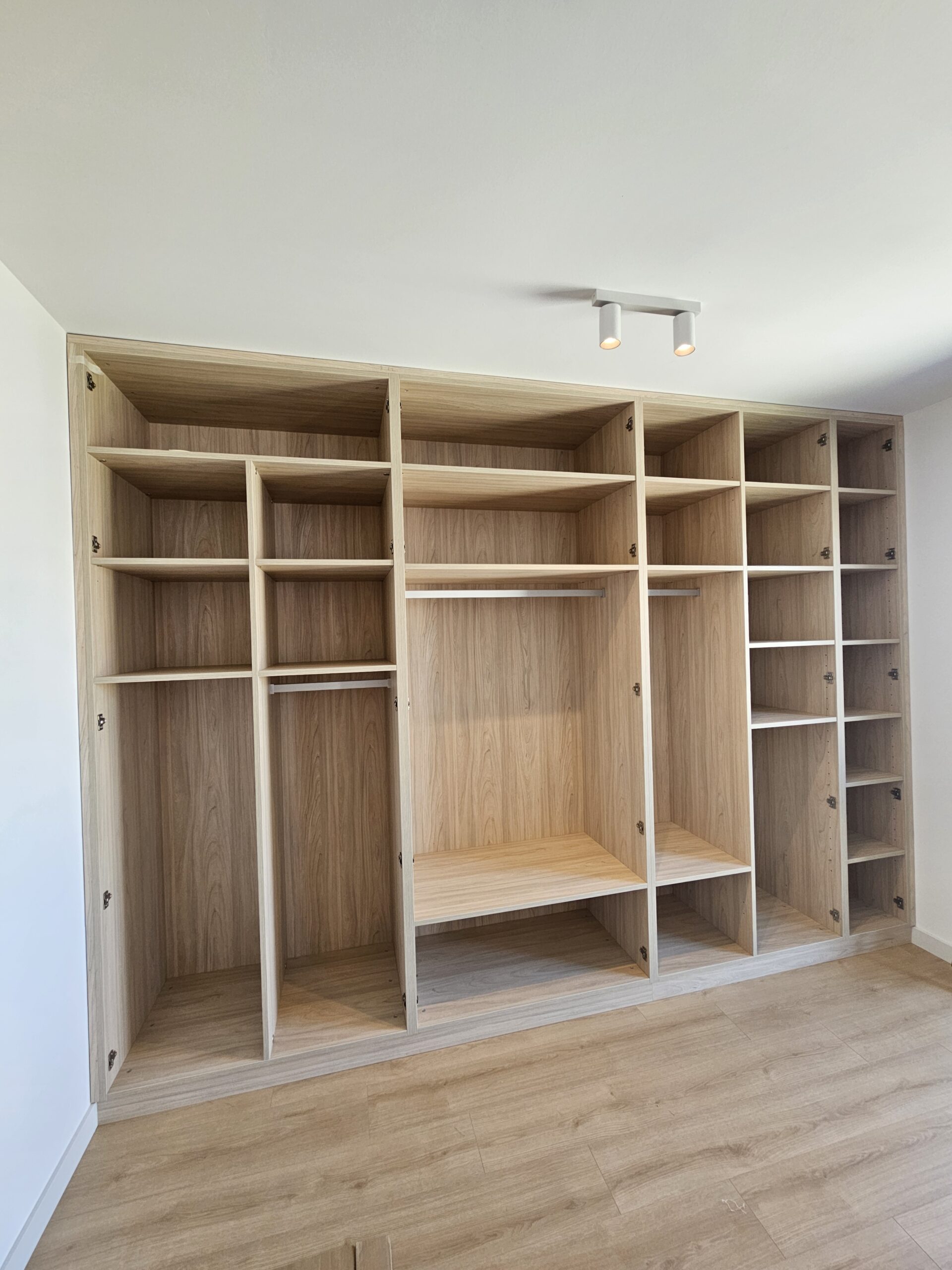 interior-armario-martorell Armario a medida en acabado roble con módulos abiertos y baldas regulables.