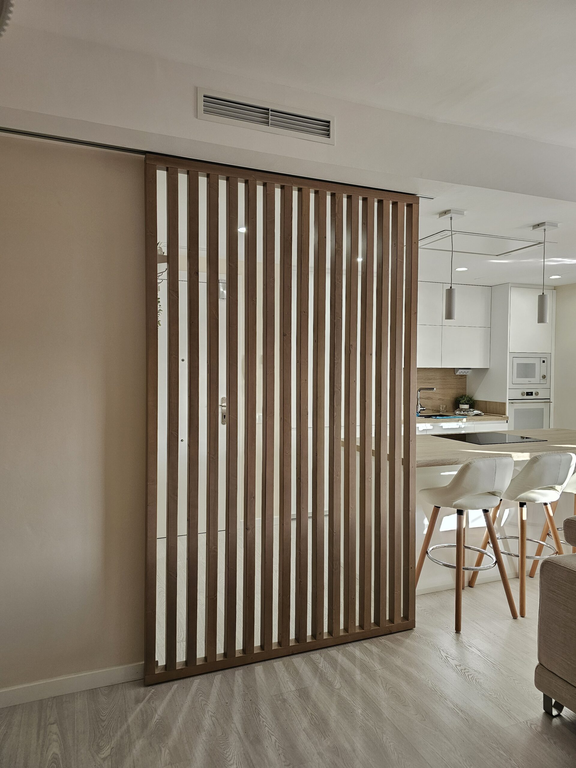 separador-madera-listonado Separador de ambientes con lamas de madera y guía corredera entre salón y cocina.